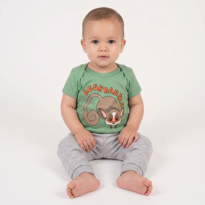 A baby wearing a green Bushbaby T-Shirt featuring a cartoon bushbaby graphic on the front, paired with plain grey pants.