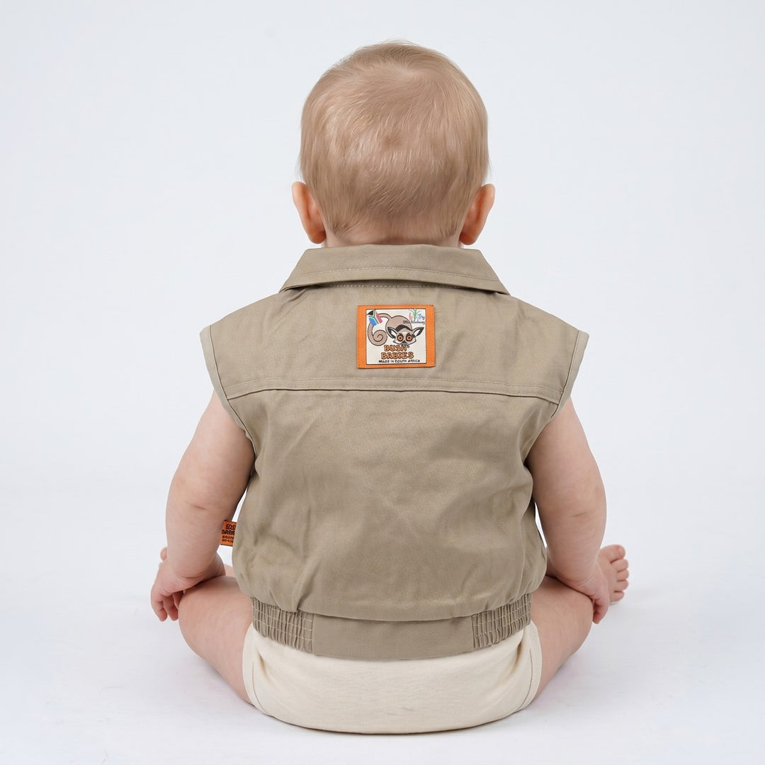 Back view of a khaki cotton canvas Bushbaby jacket for infants, featuring a collared, sleeveless design, an elasticated hem,