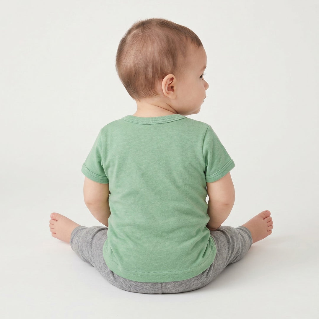Back view of a baby wearing a green Bushbaby T-Shirt and grey pants, showcasing the comfortable fit and fabric.