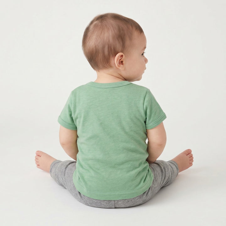 Back view of a baby wearing a green Bushbaby T-Shirt and grey pants, showcasing the comfortable fit and fabric.