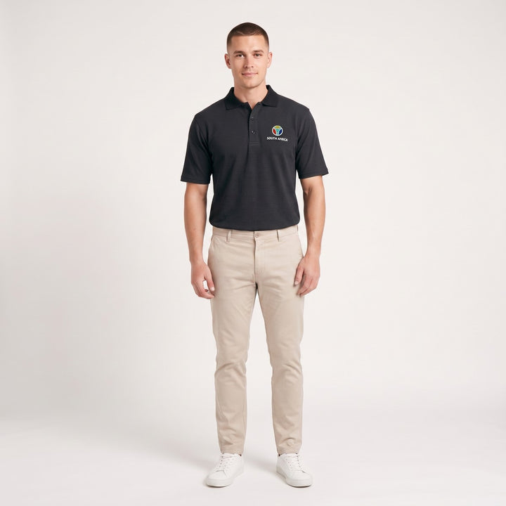 A male model wearing a black birdseye polo shirt with a South Africa logo, paired with grey pants and white sneakers.