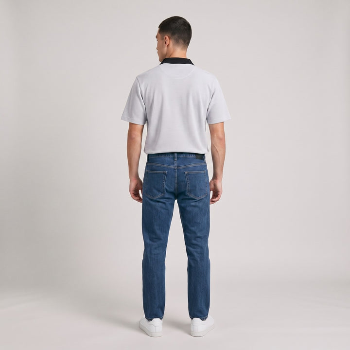 Rear view of a male model wearing a Golfer SA Birdseye White short-sleeve polo shirt, paired with blue jeans and white