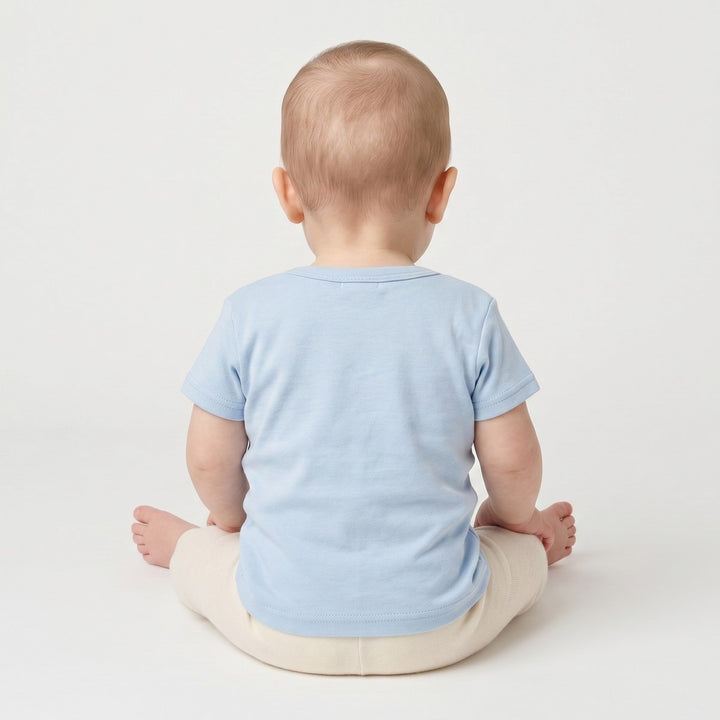 Light blue infant short-sleeve t-shirt with a crew neck, seen from the back on a baby wearing cream leggings.